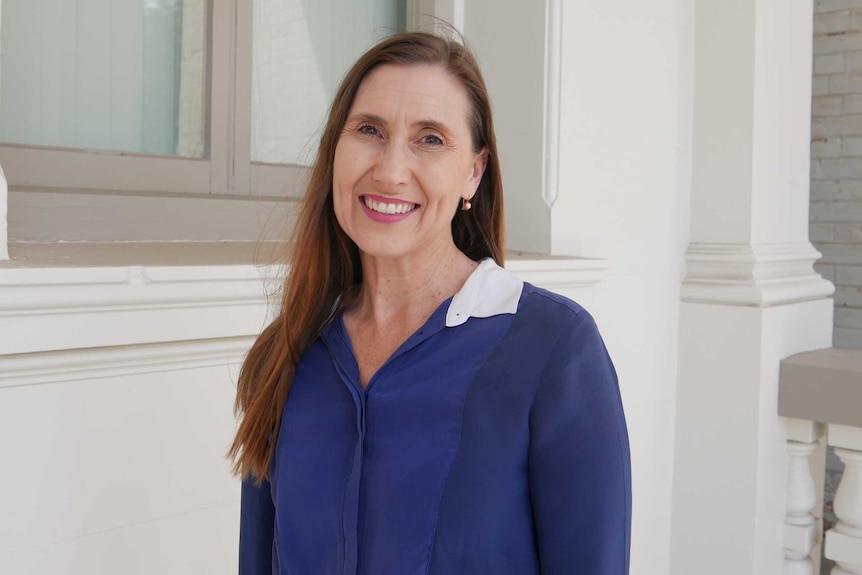 A woman with brown hair smiles. She is wearing a navy shirt.