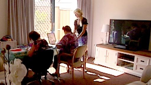 Two residents working at a desk as support staff person looks on.