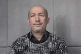 A screenshot from a video of Uyghur musician Abdurrehim Heyit wearing black and white sweater sitting against grey concrete wall