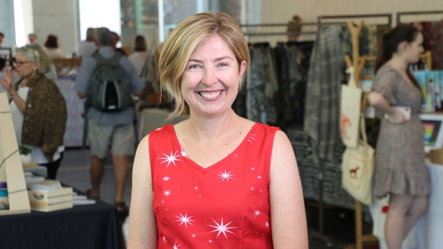 A woman with short blonde hair and a red dress stands in the middle of a clothing store