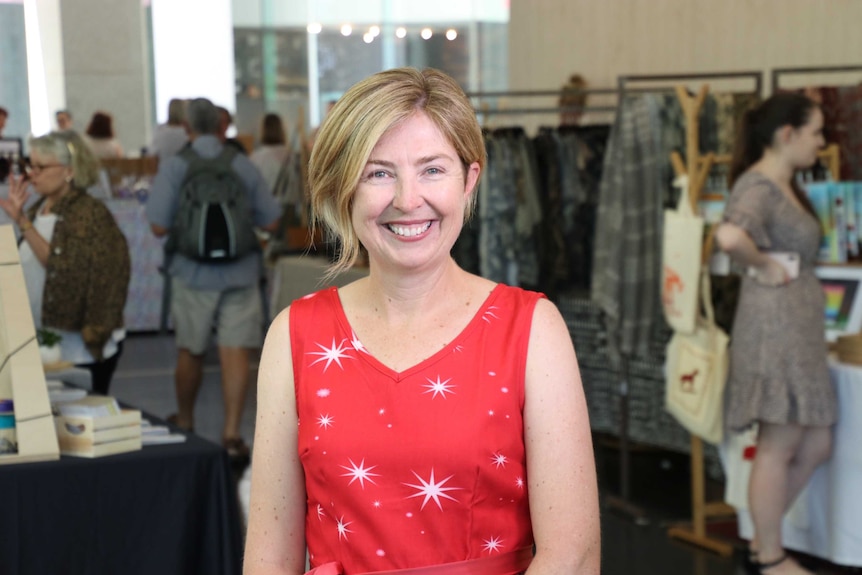 A woman with short blonde hair and a red dress stands in the middle of a clothing store