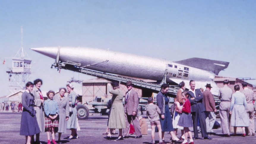 People stand in front of a V-2 rocket.
