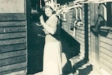 Black and white photograph of sixteen-year-old Anne Hawker standing between accommodation blocks  at Bonegilla.