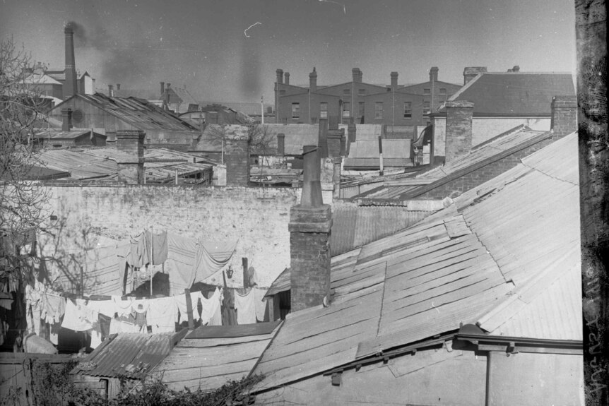 Black and white photo of the back of small houses, described as "slums", in 1916.