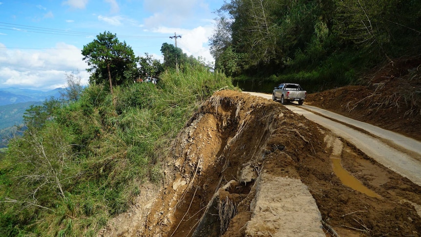A car drives a long a road next to a landslide.