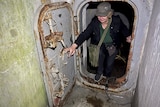 A female tour guide steps through an old hatch out of a wartime bunker.