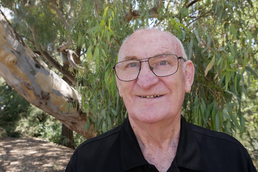 Older man, mainly bald and wearing glasses, smiles at the camera.