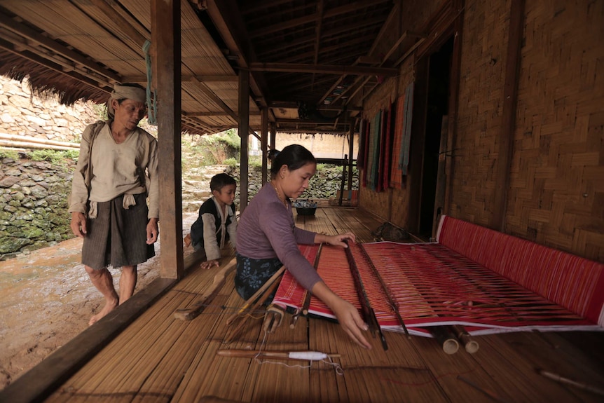 A woman sitting on the floor and weaving fabric for cloth