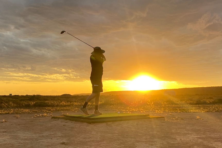 A golfer hitting a ball in front of the setting sun.