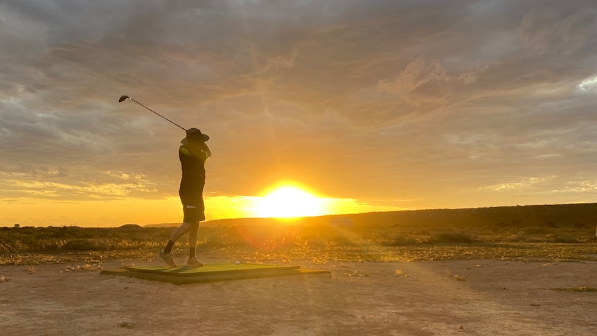 Golfer hitting a ball in front of a setting sun.