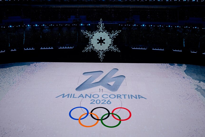 Un copo de nieve gigante cuelga en el aire sobre el suelo del estadio con la imagen de un logotipo olímpico 