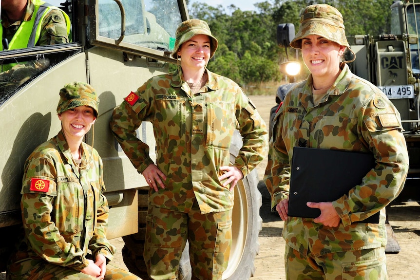 Three female soldiers stand near a truck