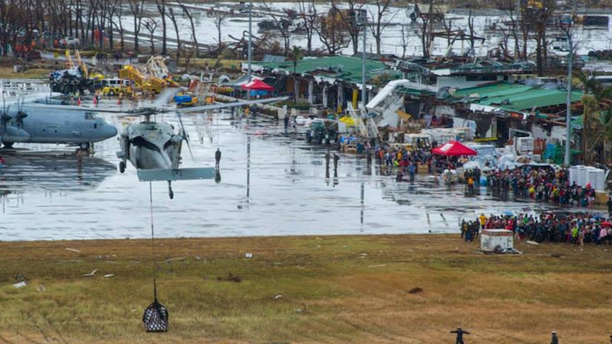 People affected by Typhoon Haiyan wait as a US Navy MH-60S Seahawk helicopter drops supplies.