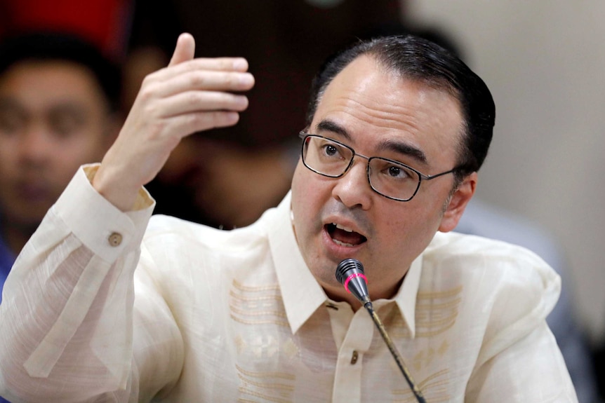 Alan Peter Cayetano speaks into a microphone and raises his hand above his head.