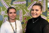 Sisters, Merinda and Sophie Dryden, standing in front of a wall painted in an Aboriginal style