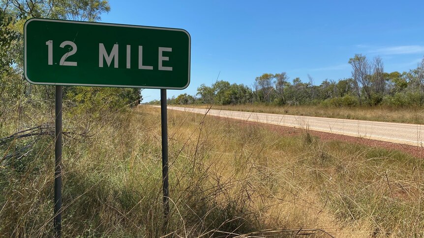 A green road sign saying "12 Mile" beside a highway.