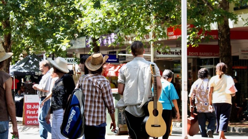 A country music fan, with guitar, walks down Peel Street