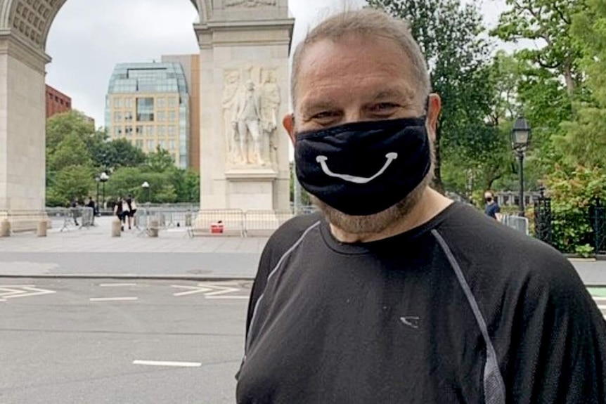 Paul Gauger wearing a black mask with a white smile on it, standing outside Central Park in New York.
