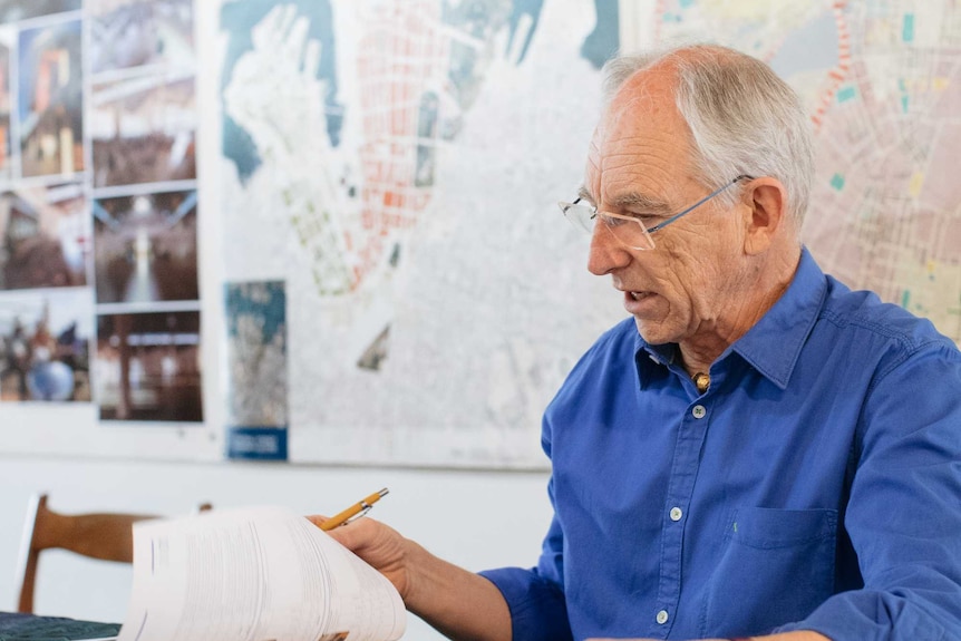 Alan Croker looks over Opera House plans with a wall of maps behind him