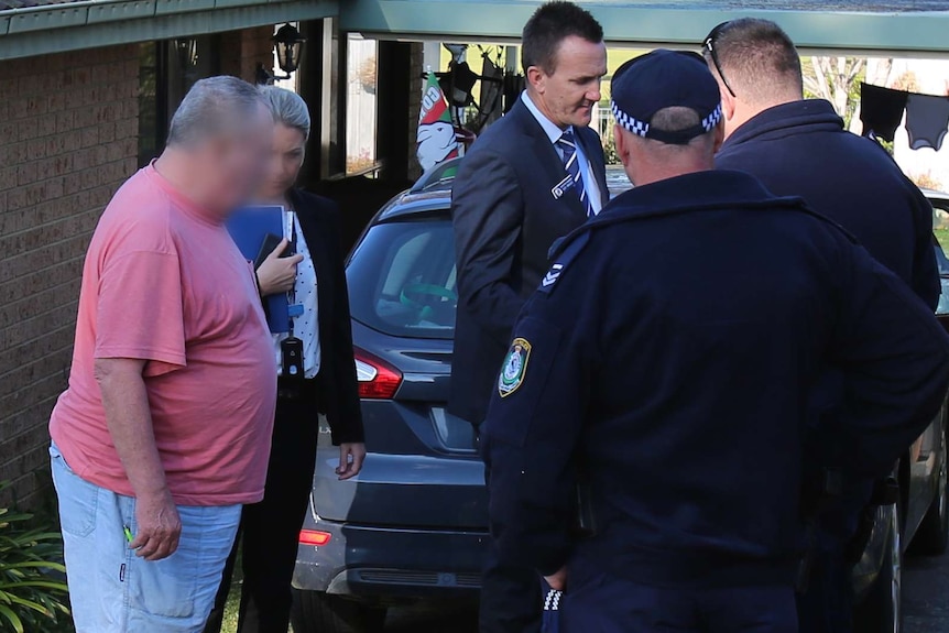 A man in a pink t-short surrounded by police officers.