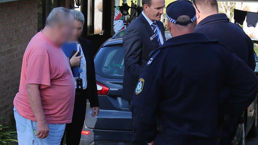 A man in a pink t-short surrounded by police officers.