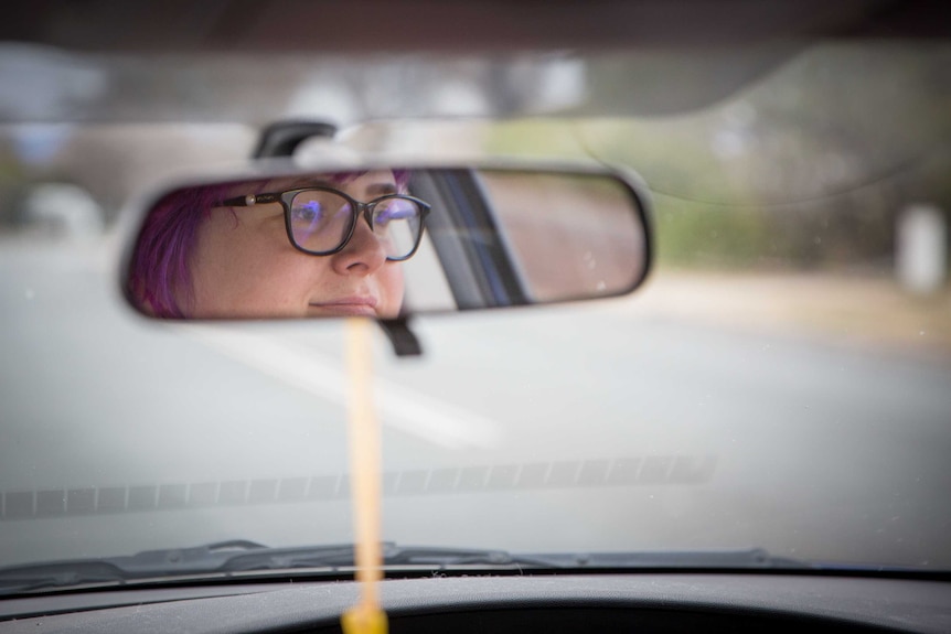 A woman's face is reflected in the rear-view mirror as she drives to work.
