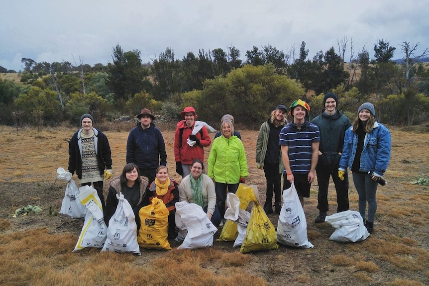 A group of 12 people stand in bushland with large bags packed full of rubbish
