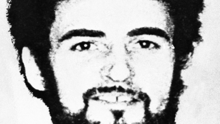 a black and white headshot of a man with a beard and a gap in his teeth looking at the camera