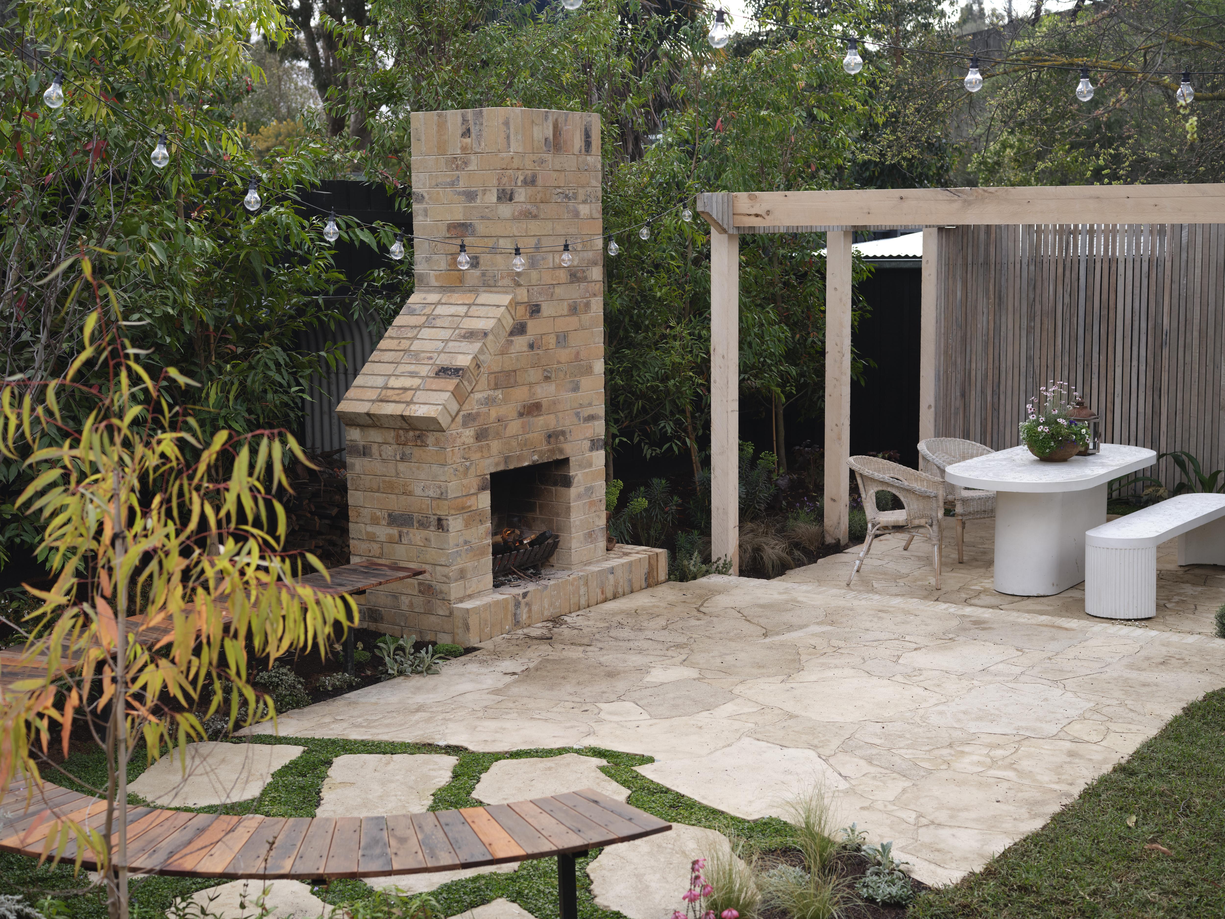 A wide shot of a backyard paved area with a fireplace and brick chimney above it