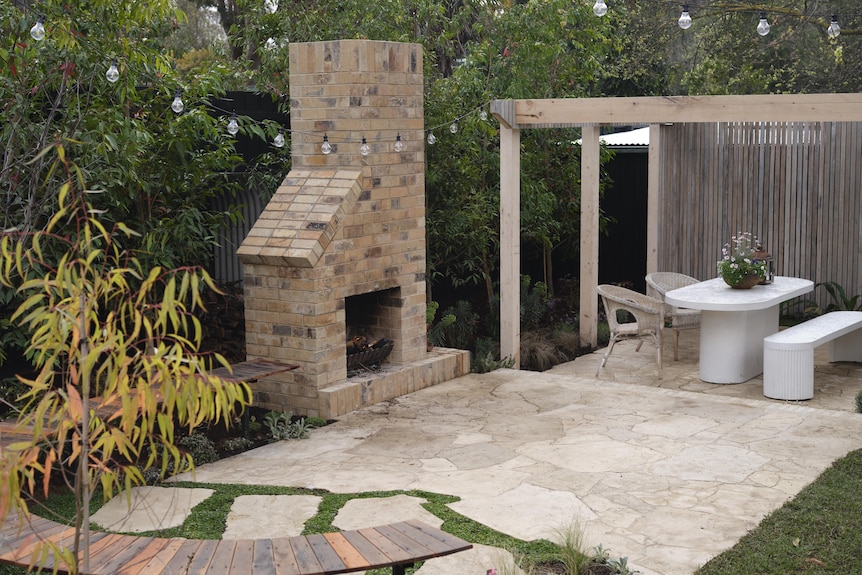A wide shot of a backyard paved area with a fireplace and brick chimney above it