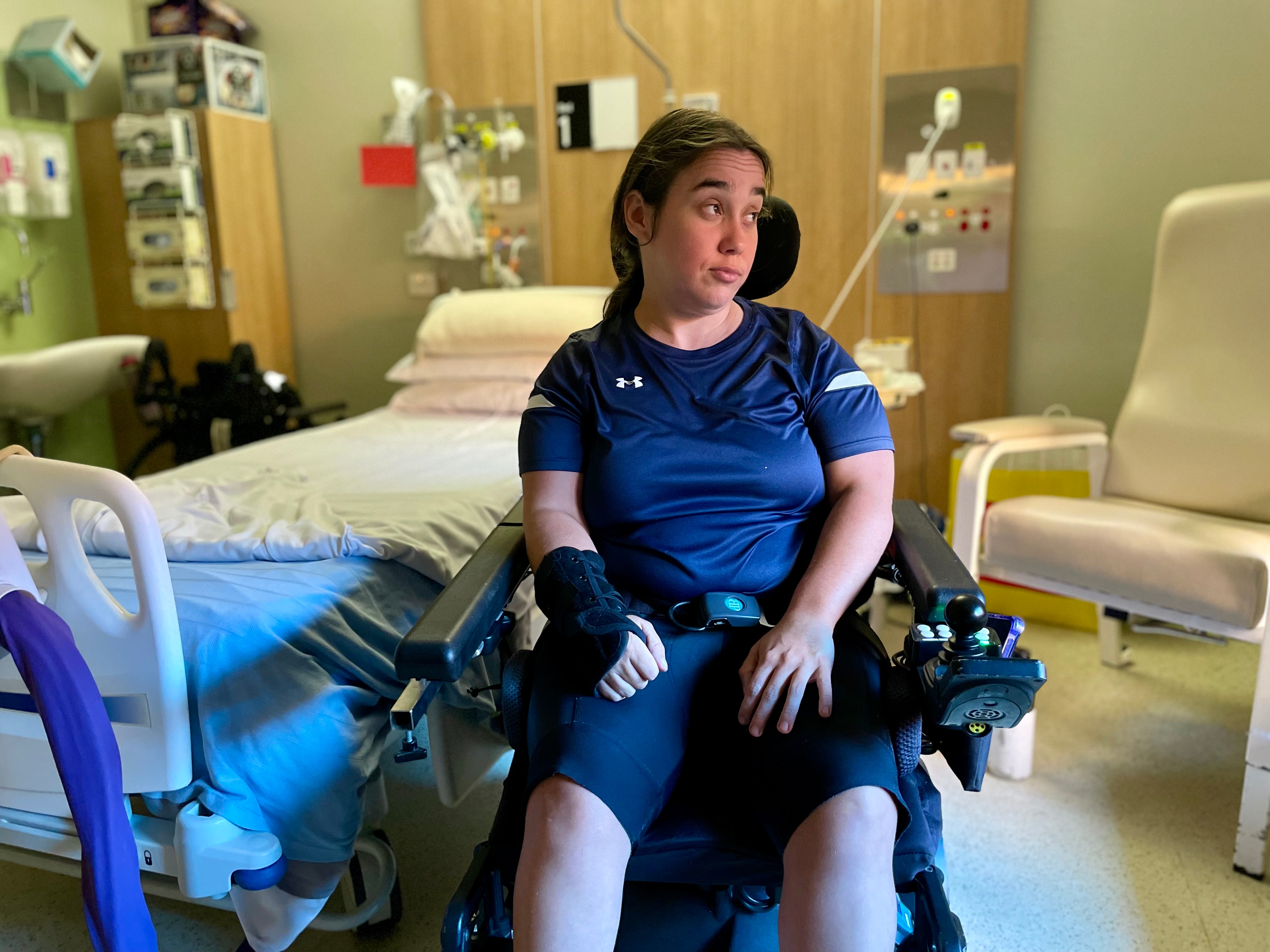 a woman in a wheelchair inside a hospital room with flowers and hospital food