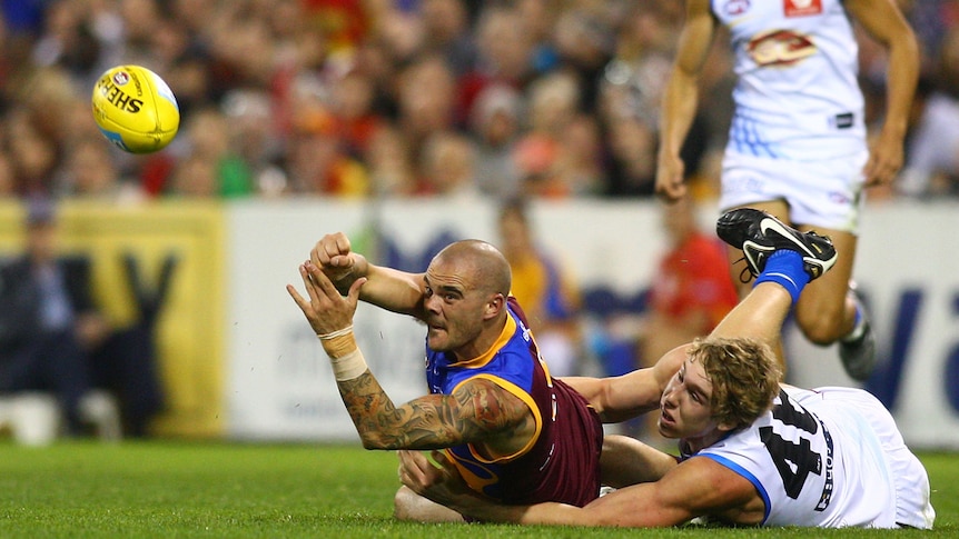 Lions defender Ashley McGrath gets a pass away while being tackled by the Suns' Tom Lynch