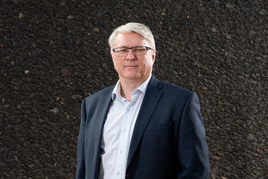 Professor Iain Young standing in front of a stone embedded wall.