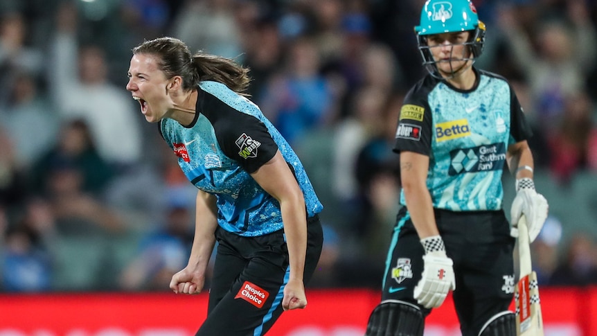 A woman with her mouth wide open and her fists clenched by her sides, wearing a cricket uniform.