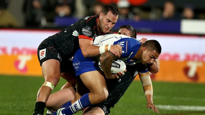 A Bulldogs player is dragged down by two Warriors players