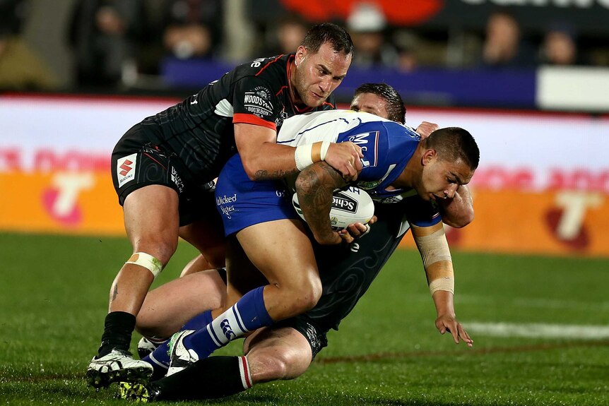 A Bulldogs player is dragged down by two Warriors players