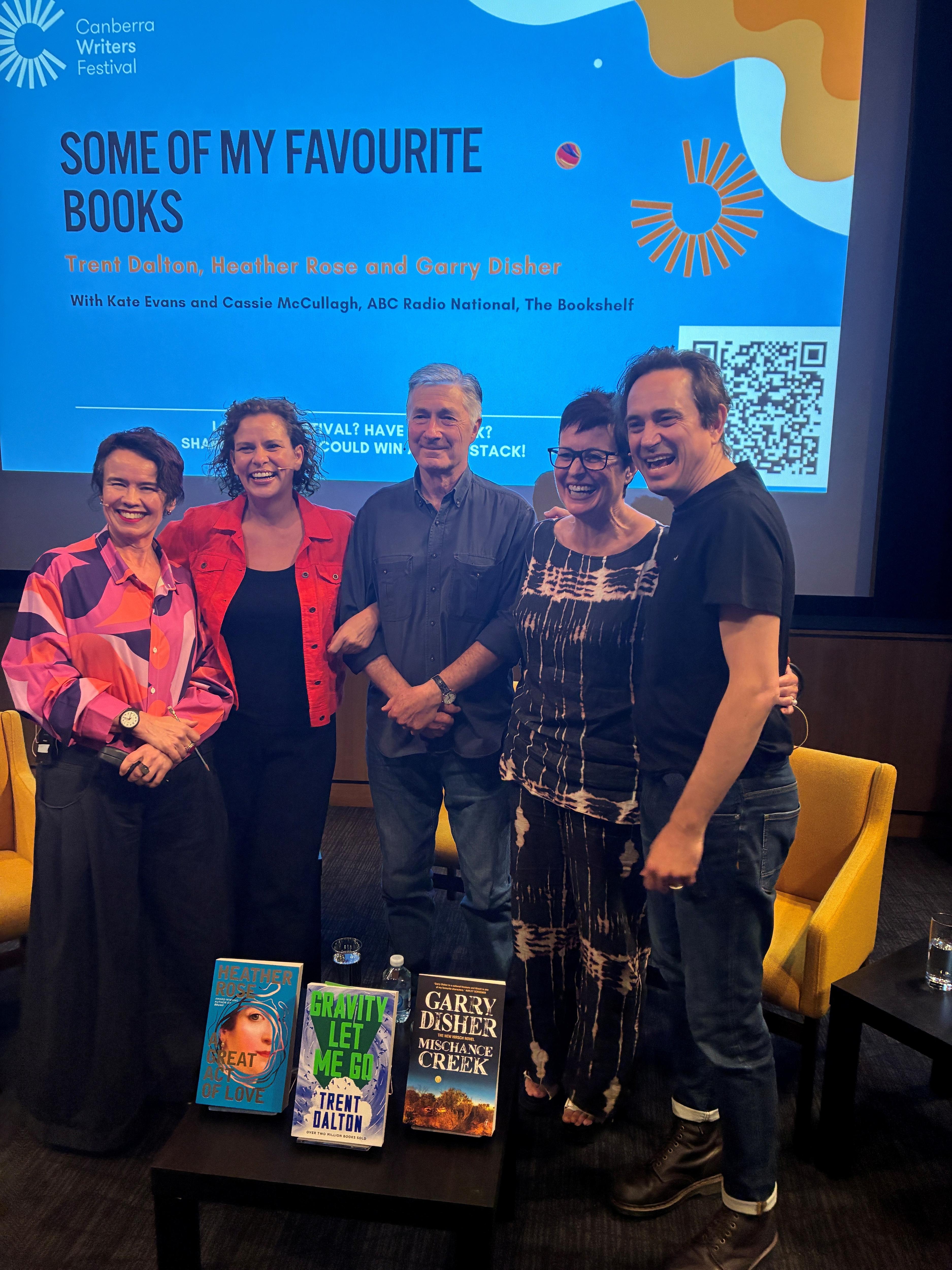 Four people beaming at the camera, arms linked, onstage. NAmes in caption