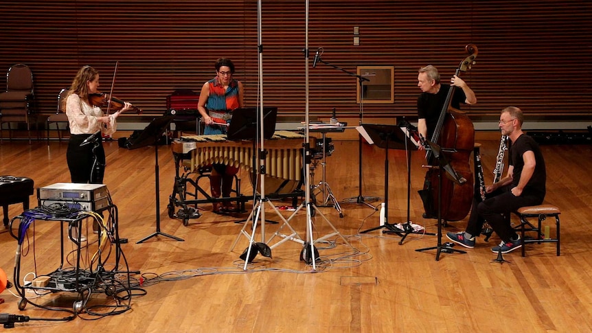 Four musicians in a recording studio playing violin, vibraphone, double bass, and bass clarinet.