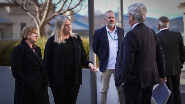 Two women speaking to a man in a suit in a forecourt.