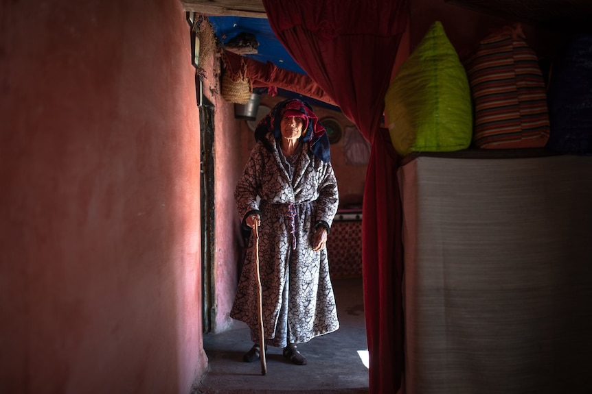 An older woman in a headscarf and holding a cane.