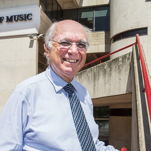A man with glasses outside a building signed 'School of Music'.