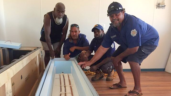 Aboriginal men gather around a number of spears, some are smiling at the camera.