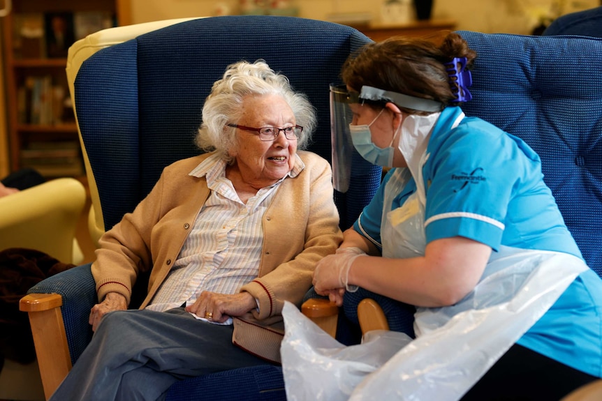 An elderly woman talks to a care worker in full PPE