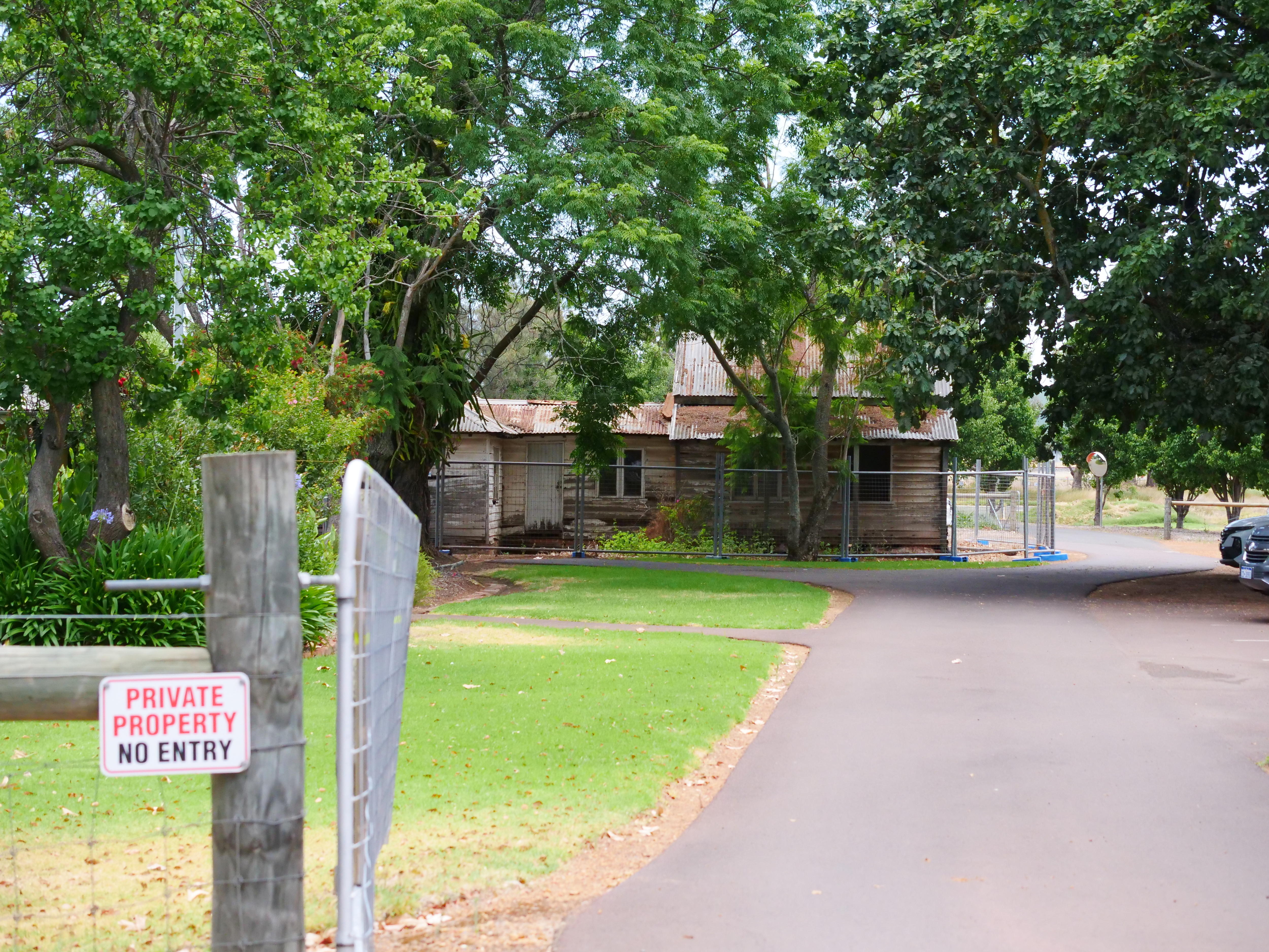 Driveway leading up to a deteriorating weatherboard building. Sign in foreground reads Private Property No Entry