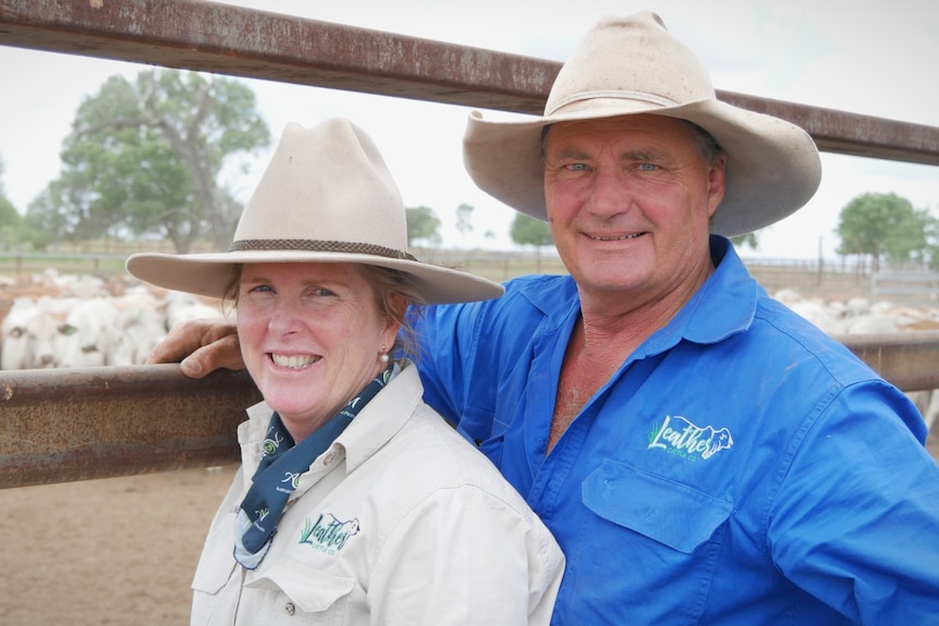 A man and woman standing in front of cattle pen wearing hats and smiling