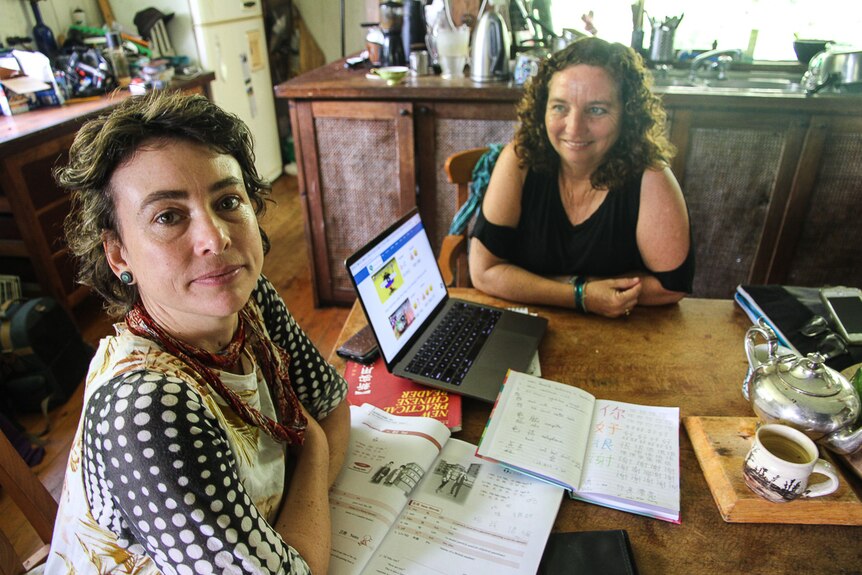 Two women sit with a laptop and exercise books during a Mandarin lesson