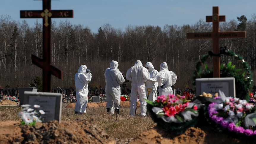 People in protective gear dig a grave at a graveyard.