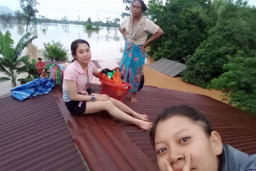 Women sit on the roof of a house, surrounded by flood waters.