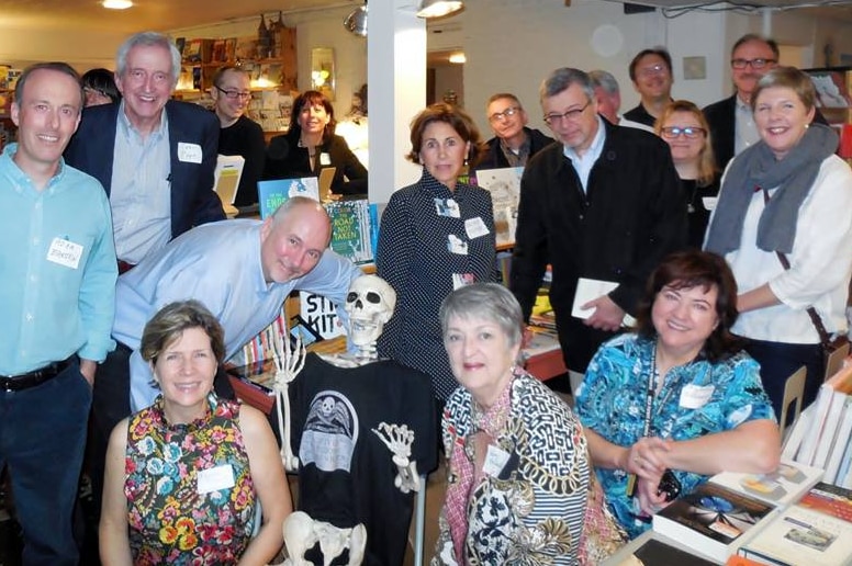 A group of obituary writers pose with a skelton wearing a society of obituary writers t-shirt.