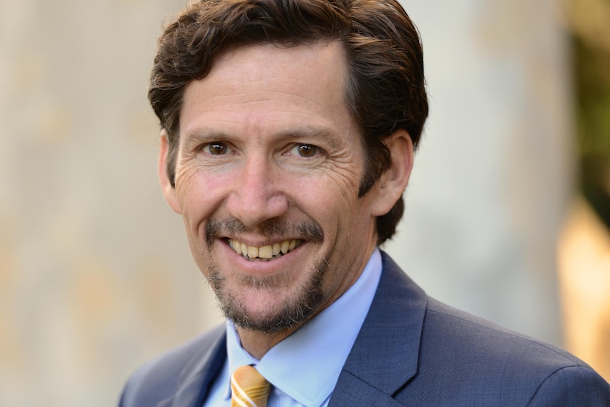 A man with brown hair and brown eyes in a suit smiling at the camera